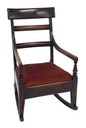 An early 19thC mahogany low rocking chair, with a ladderback, shaped arms, and a drop in seat,...