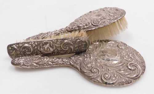 An Elizabeth II silver backed three piece dressing table set, embossed with masks, flowers and...