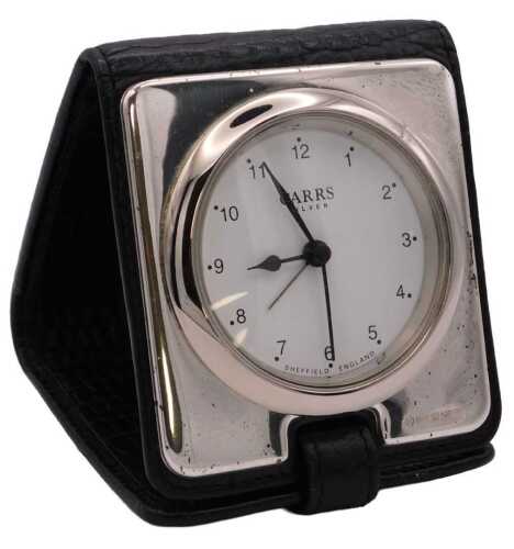 An Elizabeth II silver backed travel clock, circular white dial bearing Arabic numerals, centre...