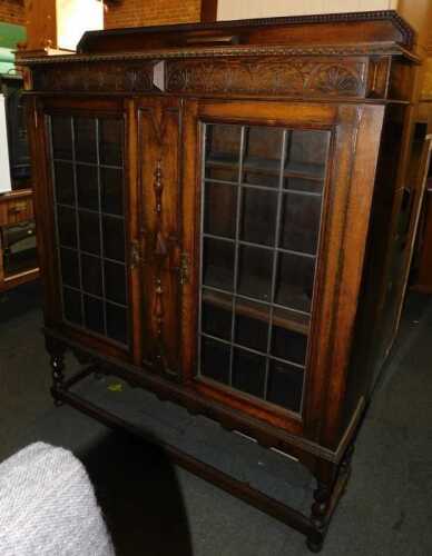 An oak display cabinet, with a raised back above two leaded glazed doors, enclosing three...
