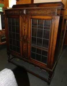 An oak display cabinet, with a raised back above two leaded glazed doors, enclosing three...