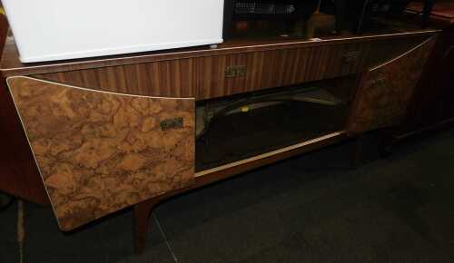 A mid century formica sideboard, with central drawer above two sliding glass doors flanked by...