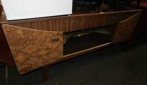 A mid century formica sideboard, with central drawer above two sliding glass doors flanked by...