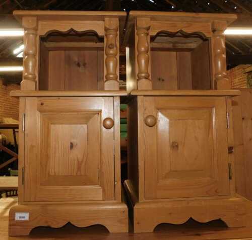 A pair of pine bedside tables, each with a recess above a panelled door, raised on bracket feet,...