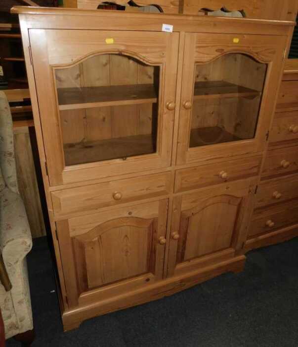 A contemporary pine display cabinet, the top with two arched glazed doors enclosing a single...