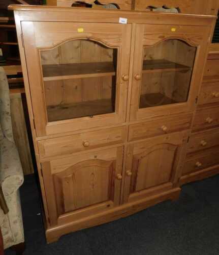 A contemporary pine display cabinet, the top with two arched glazed doors enclosing a single...