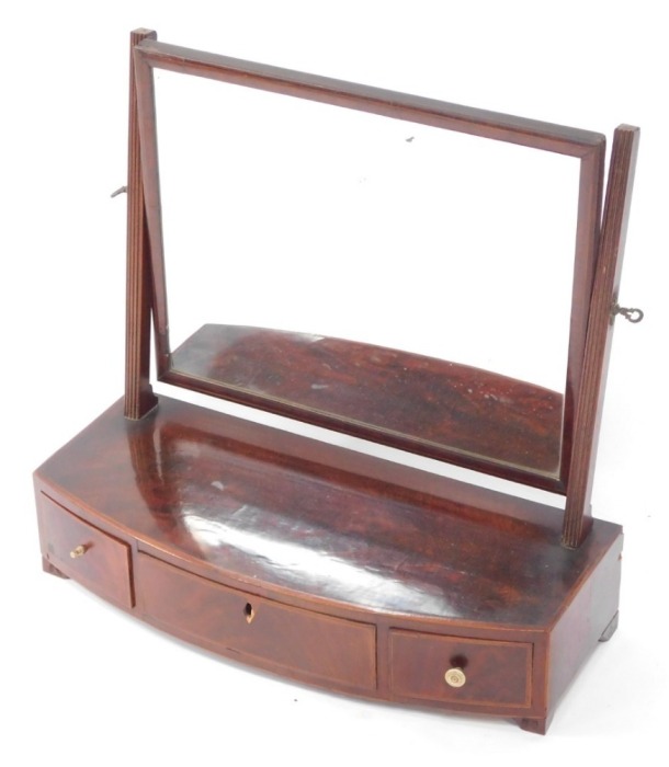 A George III flame mahogany and satinwood cross banded toilet mirror, the rectangular swing frame mirror above a bow fronted base, having one long and two short drawers, raised on bracket feet, 54cm high, 57cm wide, 24.5cm deep.