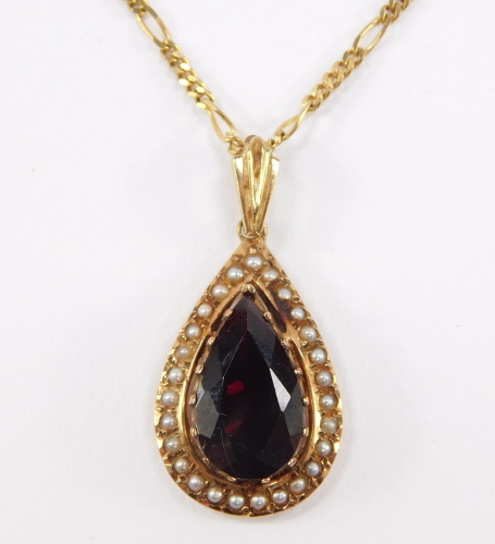 A Continental pendant, having pear cut garnet, surrounded by seed pearls, surmounted by fluted fitting, in yellow metal, with associated Italian fancy link chain marked 9ct, total length 53cm .