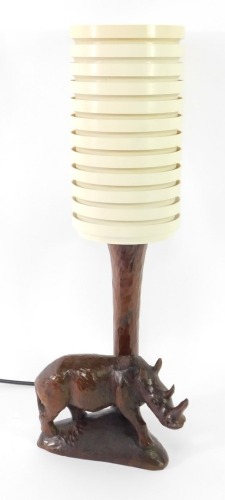 A mid century wooden table lamp carved with a rhinoceros, with a banded cream plastic cylindrical shade, 58cm high.