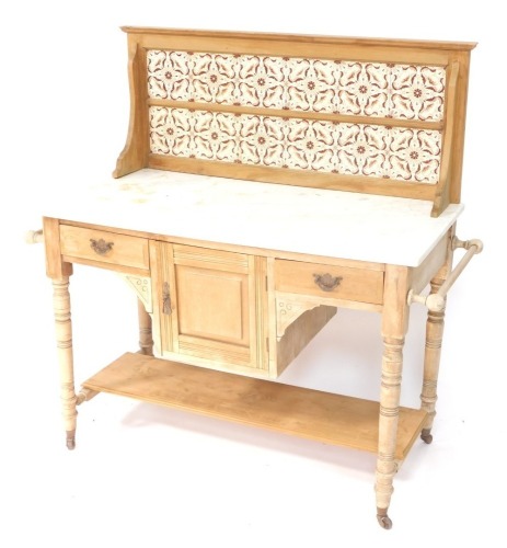 A Victorian stripped walnut washstand, the raised back with brown printed Art Nouveau style tiles, above a white marble top, and an arrangement of two frieze drawers, paneled door, and an under tier, on turned tapering legs with castors, 107cm wide.