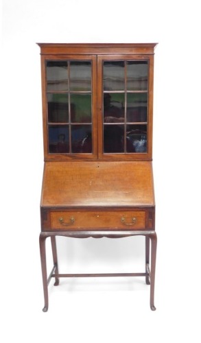 An Edwardian mahogany and satinwood cross banded bureau bookcase, the out swept pediment over a pair of glazed doors enclosing two shelves, above a fall flap opening to reveal an arrangement of three drawers and eleven recess, pen tray and two glass inkwe