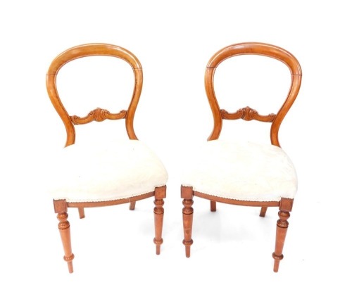 A pair of Victorian balloon back chairs, each with heavily carved horizontal scroll splats, and overstuffed seats in cream material, on turned front legs, 86cm high. (2)