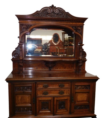 A late 19thC/ early 20thC oak and burr oak sideboard, the raised back with an egg and dart moulded cornice, above a rectangular bevelled mirror plate, with a shaped shelf on turned fluted columns, the brackets carved with fish etc., the bow fronted base w