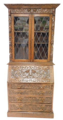 A late 19th/ early 20thC carved oak bureau bookcase, the top with a canted cornice, above a frieze decorated with scrolls, dragons heads etc., above two leaded glazed doors enclosing shelves, the base with a fall enclosing a fitted interior, above four gr