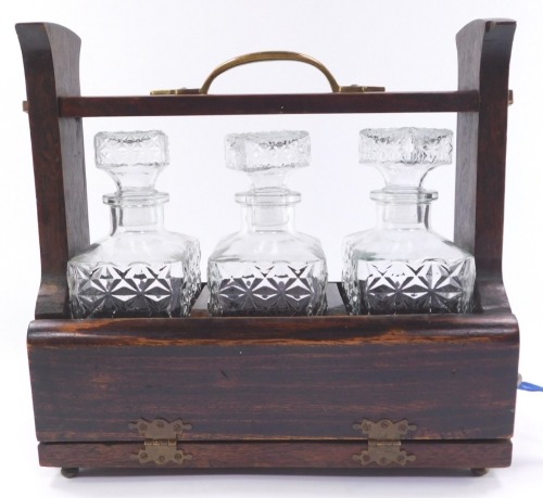 A stained pine mid century three bottle tantalus, containing three pressed glass decanters and stoppers, with key, 31cm high, 32cm wide.