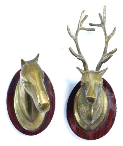 A pair of brass wall plaques, modeled as a stag's head and a horse's head, raised on oval wooden plaques, 7.5cm wide.