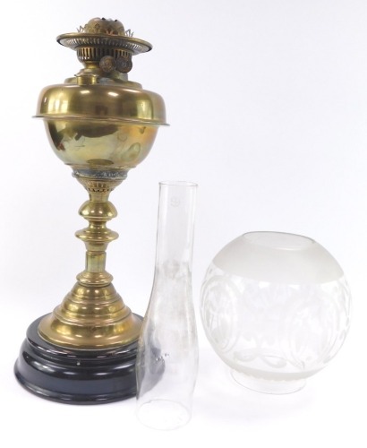 An early 20thC brass oil lamp, raised on a turned black socle, with chimney and etched globular glass shade, 67cm high.