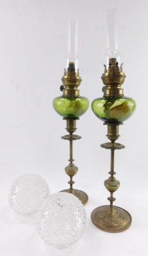 A pair of early 20thC brass oil lamps, with cast candlestick bases, ribbed green glass reservoirs, clear chimneys and hob nail cut shades, 47cm high.