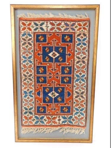 A Persian style rug, with a geometric design in cream, burnt orange, blue, etc., with fringed ends, framed, the rug 126cm x 78cm.