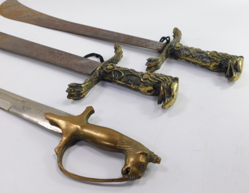 Three Eastern swords, to include a pair of short swords, each with a brass handle cast with a birds head, scrolls, etc., the blades engraved with a crocodile motif, and a sword with a curved blade, the brass handle with lion pommel, stamped made in India.