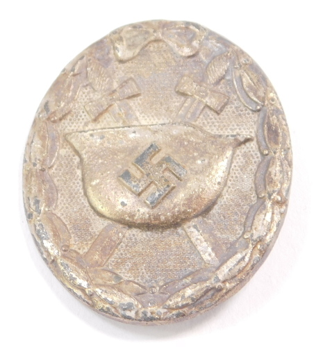A Third Reich silver wound badge, cast with a helmet and crossed swords, lacking pin.