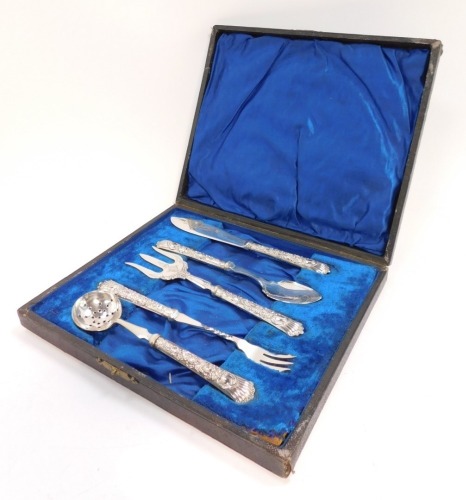 A George V silver handled serving set, with embossed rococo scroll and foliate decoration, cased, comprising butter knife, jam spoon, ham fork, pickle fork, and sugar sifting spoon, Sheffield 1911.