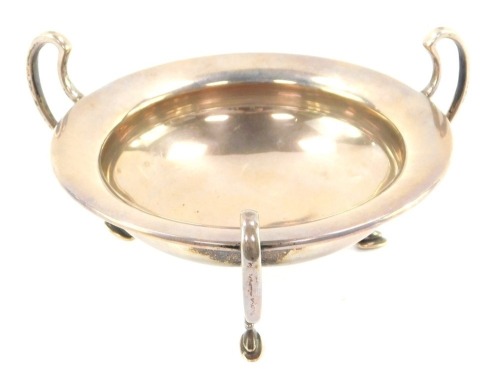A George V silver circular sweet meat dish, with three S scroll handles, raised on hoof feet, London 1915, 3.86oz.