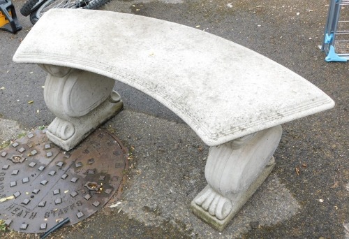 A reconstituted stone curved garden bench, raised on scroll ends supports.