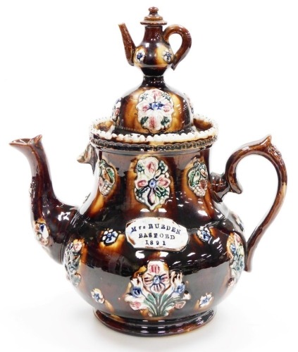 A late 19thC bargeware treacle glaze teapot, titled Mrs Burden, Basford and dated 1891, with a miniature teapot finial, the body decorated with flowers, etc., 33cm high.