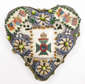 A forget me not sweetheart pin cushion, in the form of a heart with central crest for the King's Royal Rifle Corps, with outer beaded details and green pom poms, 18cm high, 18cm wide.