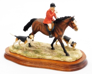 A Border Fine Arts hunting figure group, of a hunter on horseback with horn and two hounds, on a wooden base, 21cm high, 29cm wide.