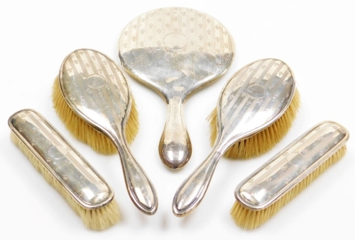 A George V silver mounted dressing table set, comprising two hair brushes, two clothes brushes and a mirror, decorated with engine turned decoration, vacant cartouche and all over crest pattern, Birmingham 1919.