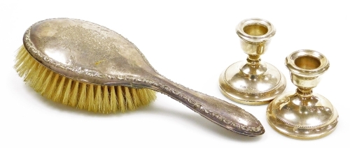 A pair of Elizabeth II silver dwarf candlesticks, of plain form with a beaded border, bases loaded, Birmingham 1967, 7cm high, and a George V silver mounted brush, with bright cut decoration and a moulded scroll border, Chester 1920.