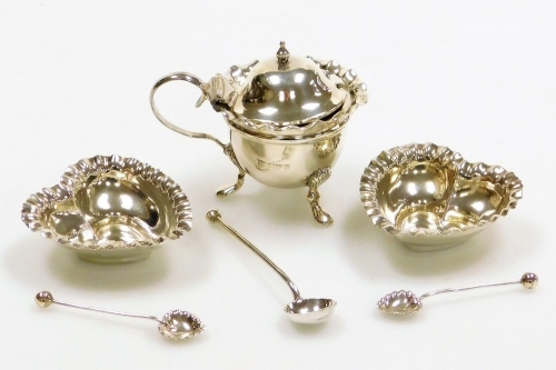 An Edward VII silver mustard pot, with a flared rim and C scroll handle, on three shell cast legs terminating in pad feet, lacking liner, Chester 1902, a silver mustard spoon, Sheffield 1878, and a pair of heart shaped open salts, with two associated spoo