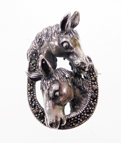 A silver and marcasite set horse brooch, with two horses heads over a horse shoe, stamped 925, with pendant loop and single pin back, 3cm high, 7.5g all in.