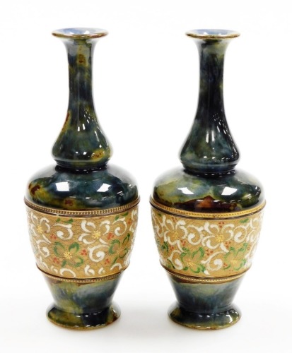 A pair of Royal Doulton stoneware bottle shaped vases, with a mottled green and blue glaze, and a floral decorated band to the centre, 23cm high.