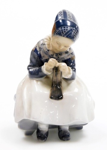 A Royal Copenhagen porcelain figure of a young girl sewing, green printed stamp and blue wave mark to underside, 14cm high.
