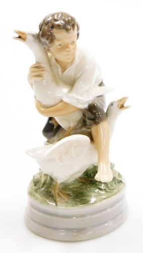 A Royal Copenhagen porcelain figure of a young boy fighting geese, on a circular base, green printed stamp and blue wave mark to underside, 18cm high.