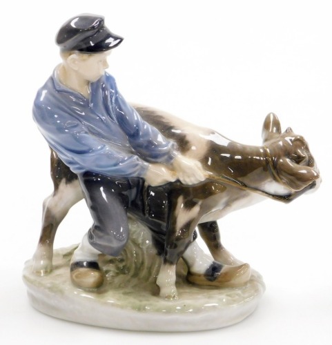 A Royal Copenhagen porcelain figure of a young boy and cow, on an oval base, green printed mark to underside and blue wave mark, 17cm high.