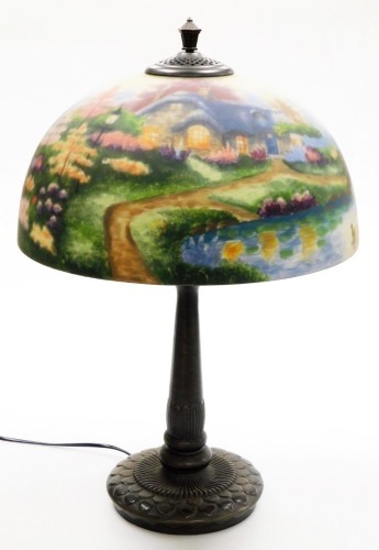 A Thomas Kinkade table lamp, the reverse decorated shade decorated with a lake and cottage scene, on a cast metal base, 57cm high.