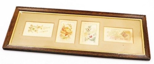 A framed set of four embroidered postcards, early 20thC war related, forget me not, etc., the frame 25cm x 64cm.