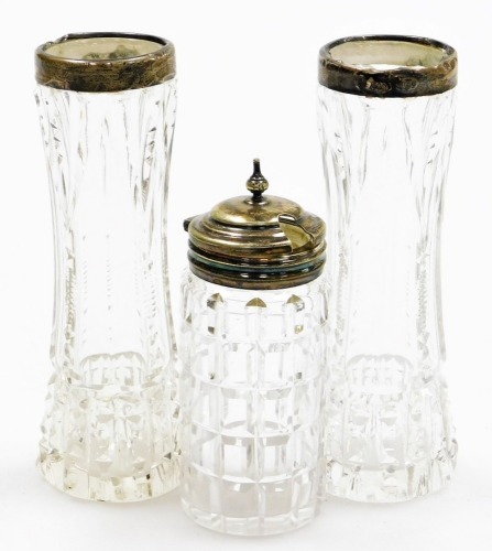 Three silver topped and cut glass jars, to include a pair of silver rimmed bud vases, and a silver plated topped in cut glass jar. (3)