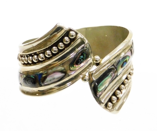 A Mexican mother of pearl set hinged bangle, of curved design, white metal unmarked, 6cm diameter.