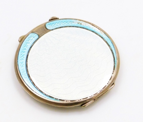 A silver and enamel compact, the front with pale blue enamel detailing, with central circle shield, with two outer fanned decoration, white metal unmarked, opening to reveal mirrored top section and compact bottom, 6cm diameter.