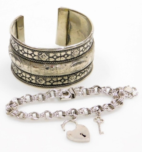 Two silver bracelets, to include a silver bangle, of hammered eastern design, and a silver charm bracelet, with two charms and heart shaped padlock, 51g all in. (2)