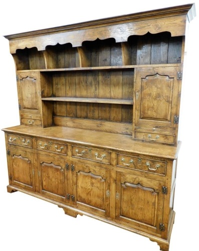An oak and elm dresser, the plain moulded top with a carved under section and four open shelves, a further open shelf flanked by cupboards, drawers and slide above four short cock beaded drawers with swan neck brass handles, and four cupboards beneath wit