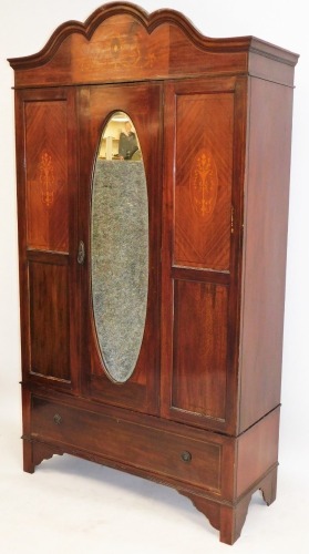 An Edwardian mahogany double wardrobe, with moulded cornice top, inlaid with marquetry neoclassical motifs, and flowers, with central oval mirror door, above a single drawer, 224cm high, 120cm wide, 46cm deep.