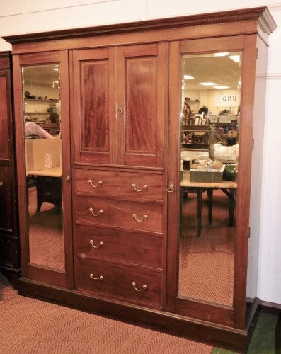 An Edwardian Maple and Co mahogany triple wardrobe, the dentil cornice raised above a boxwood inlay centred by panelled doors and drawers flanked by mirrored sections on a block base, 210cm high, 194cm wide, 47cm deep.