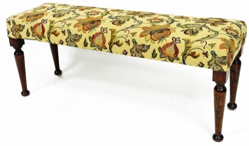 A Victorian style mahogany stained duet stool, the padded seat in floral fabric, on turned tapering legs, terminating in compressed bun feet, 47cm high, 115cm wide, 36cm deep.