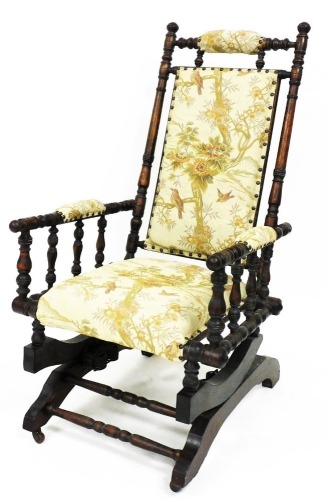 An early 20thC American style rocking chair, the turned frame with padded top, back, arms, and seat, on a rocker base terminating in front castors, 110cm high.